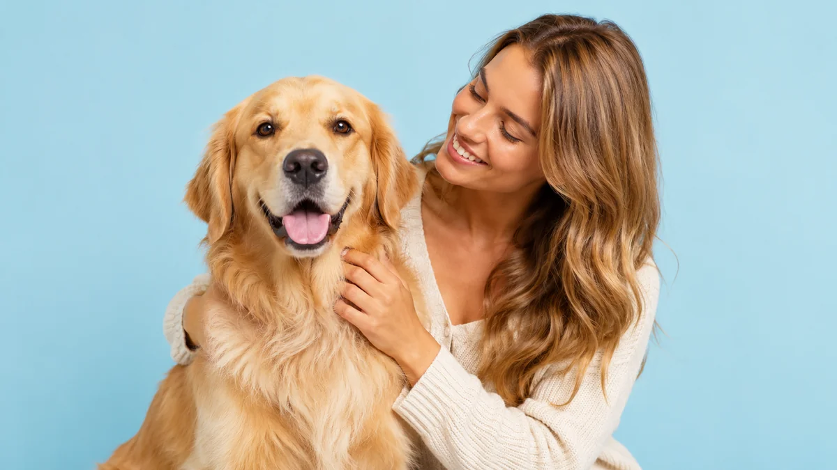 Mulher abraçando um golden retriever sobre fundo azul-claro