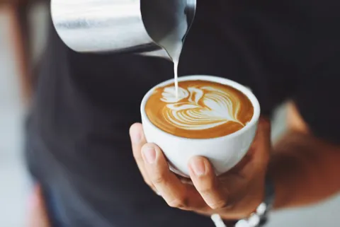Detalhe do leite sendo servido em uma xícara de café