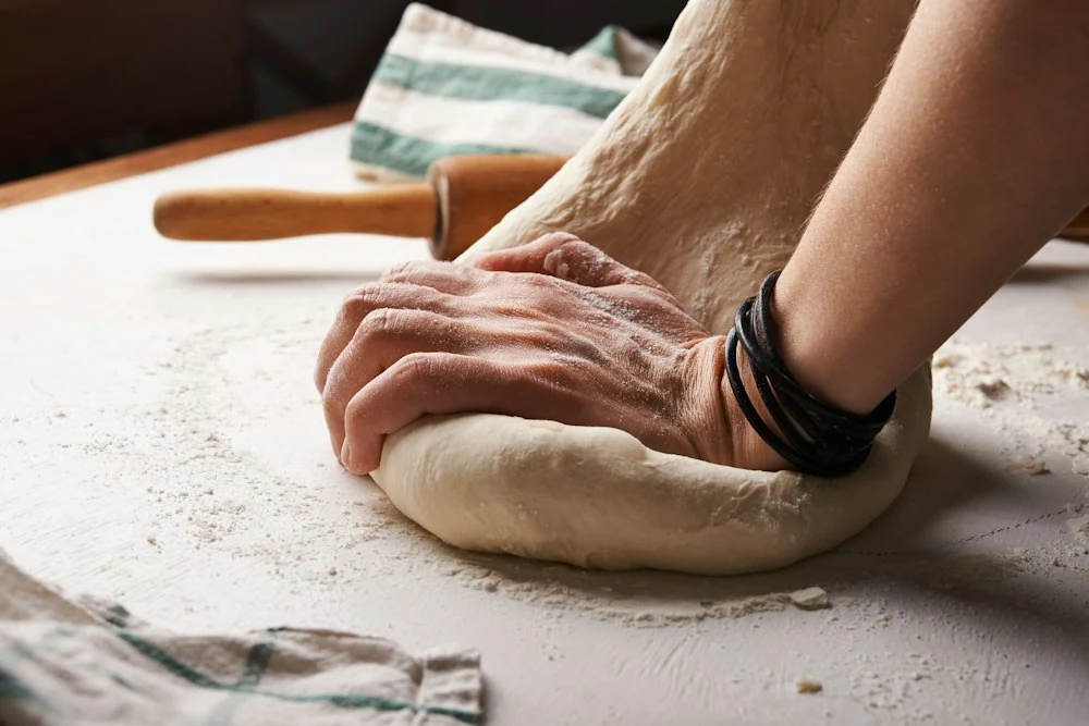 Mãos sovando a massa de pão sobre bancada enfarinhada